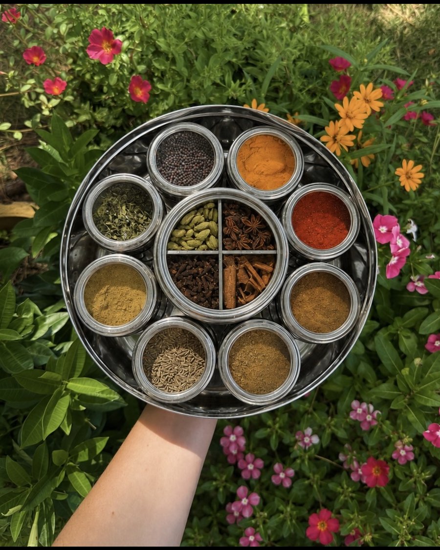 Spice Wheel masala dabba held over a flower bed, filled with whole and ground spices